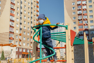 A small boy in a mask walks on the Playground during the quarantine. Stay at home