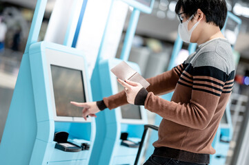 Fototapeta na wymiar Asian man tourist wearing face mask using self check-in kiosk in airport terminal. Coronavirus (COVID-19) pandemic prevention when travel abroad. Health awareness and social distancing concept