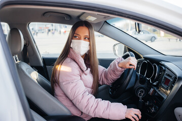 A young girl sits behind the wheel in the car in the mask during the global pandemic and coronavirus. Quarantine