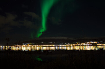 aurora borealis over arctic circle settlement reflecting in fjord water over snowy mountain