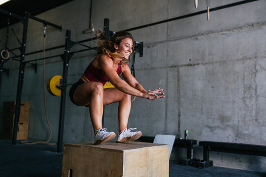 Smiling female athlete jumping onto the box