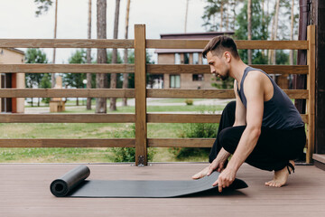 Man is going to do yoga and unfolded a yoga mat at wooden porch.