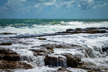 Coral reef at the edge of the sea bathed in sea foam. Small waterfalls of rocks below the horizon.