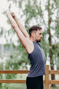 Flexible man in t-shirt rises haund up, bent back and stretches on a nature.