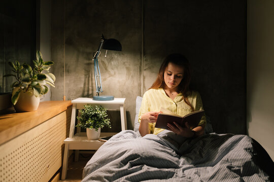 Young woman reading a book in bed