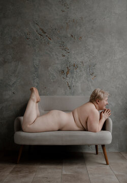 Naked woman with overweight lying on stomach on sofa.