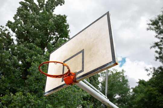 basketball court in a park with trees with white board and no net on the hoop