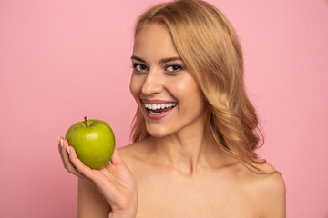 Clear strong white straight teeth stomatology concept. Portrait of attractive charming nude natural model having green apple in hand isolated on pink background