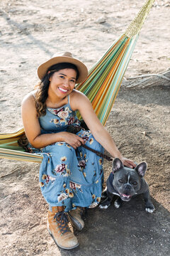 A woman sitting in a hammock with her french bulldog.