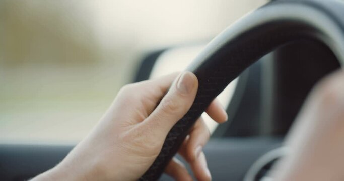 Slow motion closeup of female hands on a steering wheel.