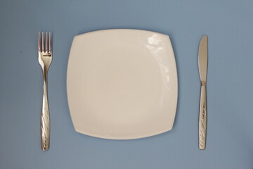 Empty plate, fork and knife over blue background. Clean plate and cutlery on light background. Top view. Flat lay.