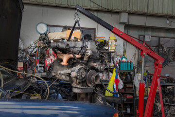 Engine hanging on crane hook on car repair service. Photo of old engine hanging on a cable. Engine hanging for overhaul.