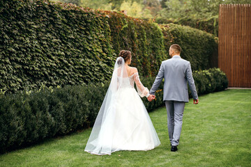 Wedding couple walking in the park holding hands, the bride and groom are smiling and enjoying each other