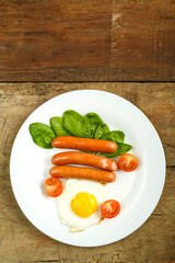 Fried egg with sausages and cherry tomatoes in a white plate on a wooden table.