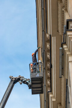 Reconstruction of the building of the Drama Theater in the city. Two working painters on an air platform paint a wall.