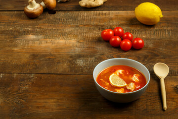 Tom yum soup with chicken in a plate on a wooden table. Copy space.