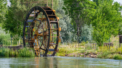 Huge water mill wheel and waterfall on river on sunny day. Sustainable energy and water power traditional machinery © attraction art