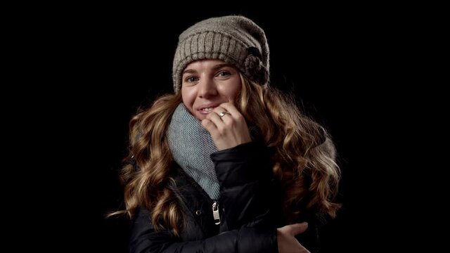 Junge blonde Frau friert im winterlicher Bekleidung vor schwarzem Hintergrund