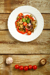 On a wooden table is a white plate masha with vegetables and mushrooms on a napkin and a fork. Copy space.