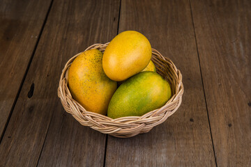 Ripe mango in basket on wooden table. Tropical fruit. Group of fresh mango. Ripe yellow mangoes on wooden background