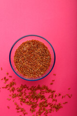 Glass jar with brown rice on a pink background.