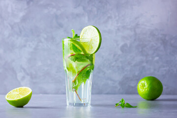 Mojito cocktail with lime and mint in tall glass. Fresh mojito in glass on a gray background. Refreshing mint cocktail with lime. Infused water