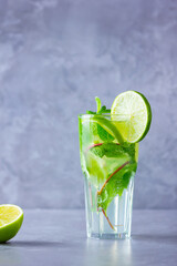 Mojito cocktail with lime and mint in tall glass. Fresh mojito in glass on a gray background. Refreshing mint cocktail with lime. Infused water