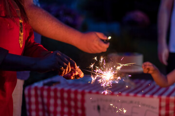 Closeup of a woman's hand lighting sparklers in the backyard at a family celebration