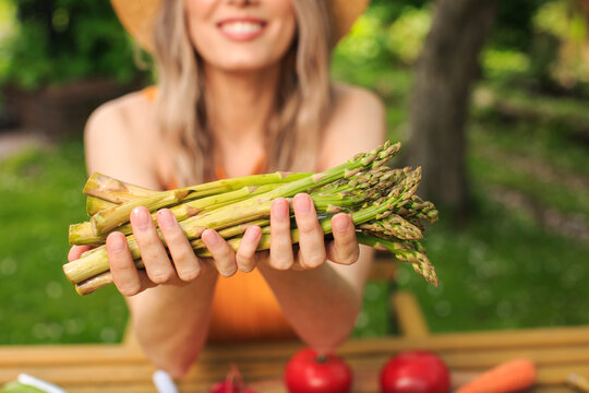Young pretty girl in a hat is sitting at wooden table with fresh vegetables grown in her garden in the summer. close up