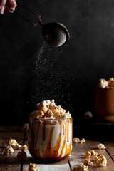 Milkshake with popcorn and caramel syrup on a black background. Sprinkle with powdered sugar.