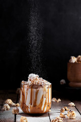 Milkshake with popcorn and caramel syrup on a black background. Sprinkle with powdered sugar.