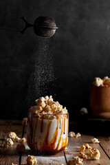 Milkshake with popcorn and caramel syrup on a black background. Sprinkle with powdered sugar.