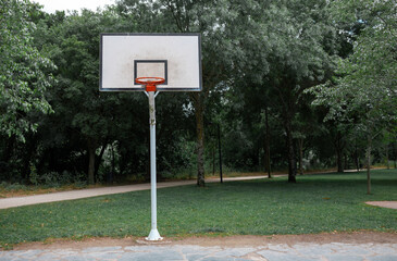 basketball court in a park with trees with white board and no net on the hoop - 360028962