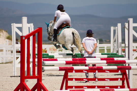 Female horse jumper being observed by her coach on a training session.