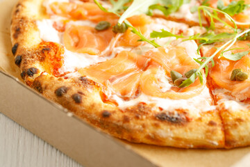 Close up of pizzas with variety of toppings and cheese in cardboard take out boxes with open lid on wooden table