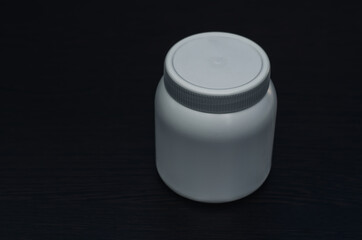White plastic jar for drugs on a dark wooden background.