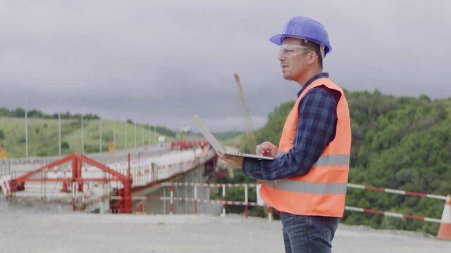 Construction engineer or an architect with a halmet and protective equipment on a building construction site using a laptop.