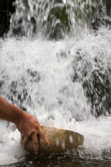 Vertical shot of hand picking up water with a big tibetan singing bowl from a waterfall.
