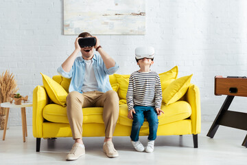 excited father and son using vr headsets while sitting on yellow sofa