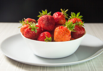 Strawberries in a white plate on the table.