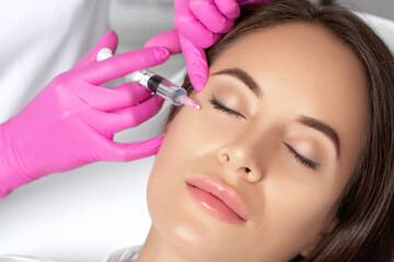 Beautiful brunette woman at the beautician.Cosmetologist does anti wrinkle injections around eyes...