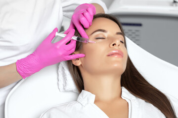 Beautiful brunette woman at the beautician.Cosmetologist does anti wrinkle injections on the face...