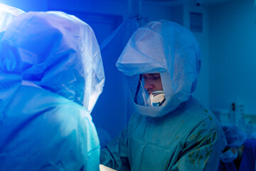 Two doctors in personal protective equipments including white suit to protect COVID 19 infection. Surgery operation.