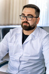 Serious doctor sitting at computer. Medical office. Doctor at work. Diagnosing. Bearded man.