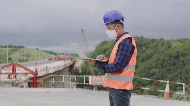 Construction engineer or an architect with a halmet and protective mask and equipment using a computer during COVID-19 virus.