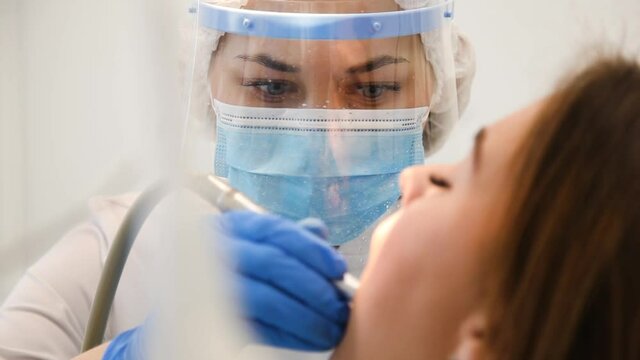 Close-up of concentrated female dentist curing tooth with plague and cavity. Patient on stomatology chair repair aching teeth. Stomatologist and patient at clinic office. Toothcare concept