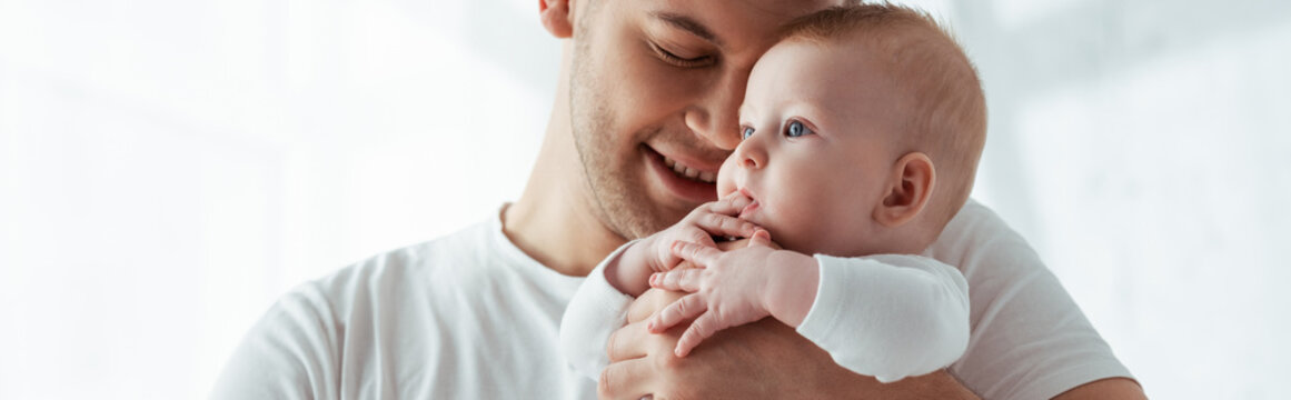 horizontal image of happy father with closed eyes holding little baby boy on hands