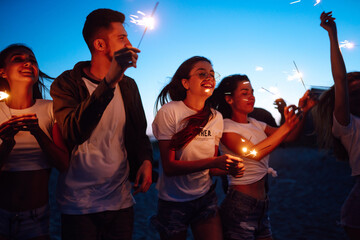 Group of young people having fun with sparklers outdoors at the sea shore. People celebrating new year's day at the beach. Beach party, rest, vacation.