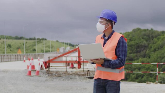 Construction engineer or an architect with a halmet and protective mask and equipment using a computer during COVID-19 virus.