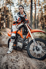 Obraz na płótnie Canvas Beautiful young brunette female racer riding motocross bike on a trail of sand in the woods